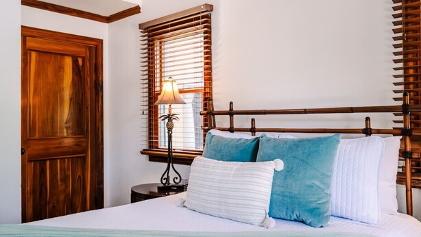 A bedroom with a wooden headboard, a bed with white and blue pillows, a bedside table with a lamp, and a wooden door. - Three bedroom  in Costa Rica, Playa Langosta (Tamarindo)