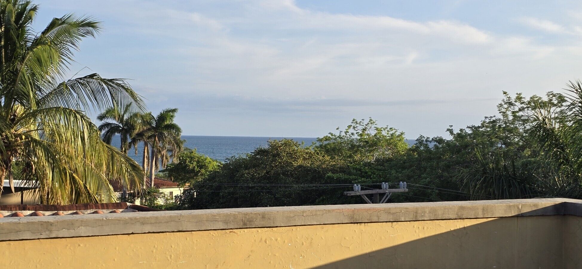 Un balcone con vista sul mare, palme e una struttura per linee elettriche.