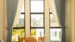Quarto de hotel com uma janela grande, uma cama, duas cadeiras e uma mesa pequena com um vaso de flores.