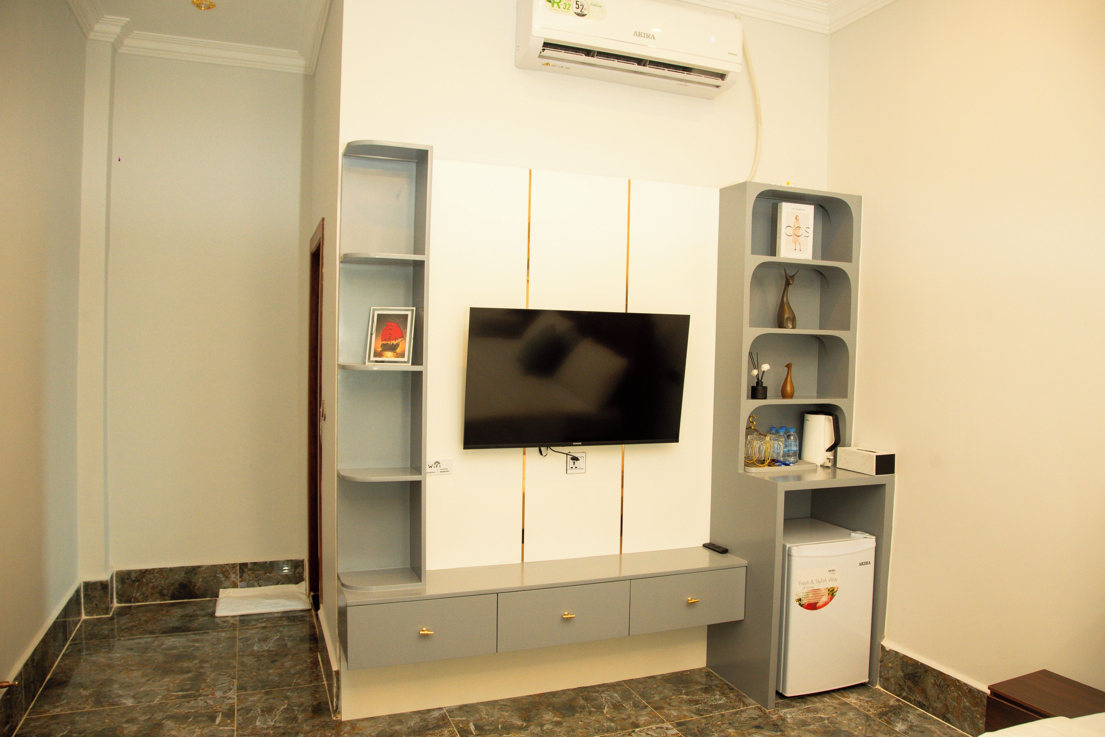 A modern living room with a flat-screen TV mounted on the wall, a built-in entertainment unit with shelves, and a small refrigerator.