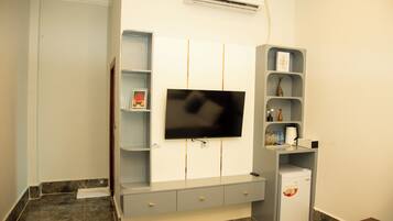 A modern living room with a flat-screen TV mounted on the wall, a built-in entertainment unit with shelves, and a small refrigerator.