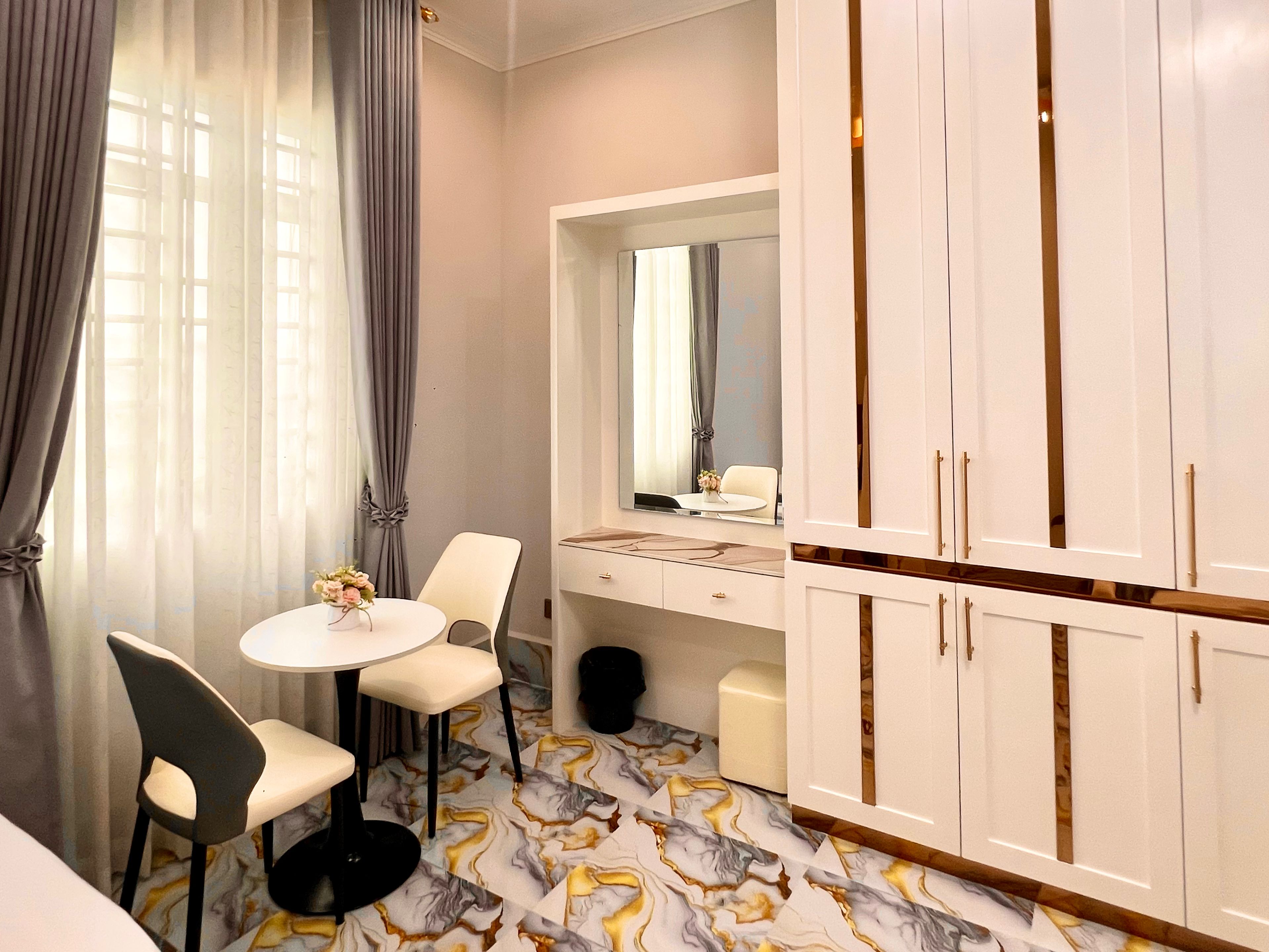 A hotel room with a bed, a round table with two chairs, a vanity with a mirror, and a wardrobe with two doors.