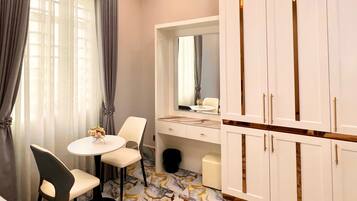 A hotel room with a bed, a round table with two chairs, a vanity with a mirror, and a wardrobe with two doors.