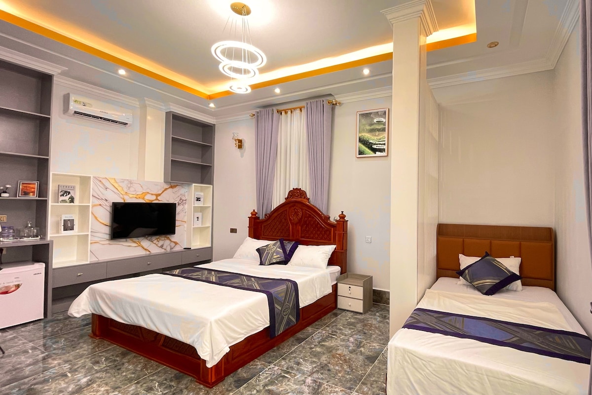 A hotel room with a large bed, a smaller bed, a TV, a wardrobe, and a marble floor.