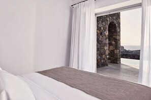 Ein Schlafzimmer mit einem Bett, weißen Vorhängen und Blick auf eine Steinsäule und das Meer.