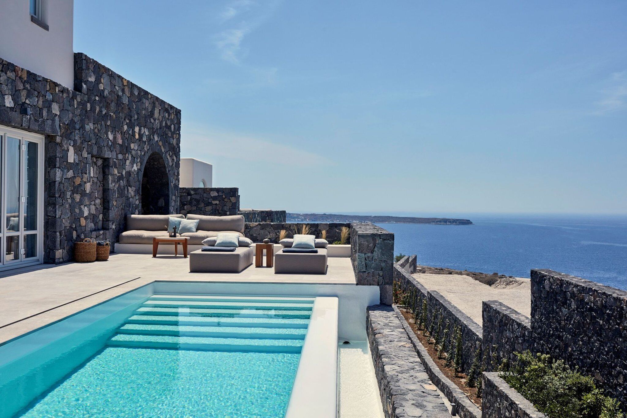 A pool area with a stone wall, outdoor seating, and a view of the sea.