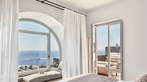 Ein Schlafzimmer mit einem großen Bogenfenster, einem Bett und Blick auf das Meer sowie eine Steinsäule.