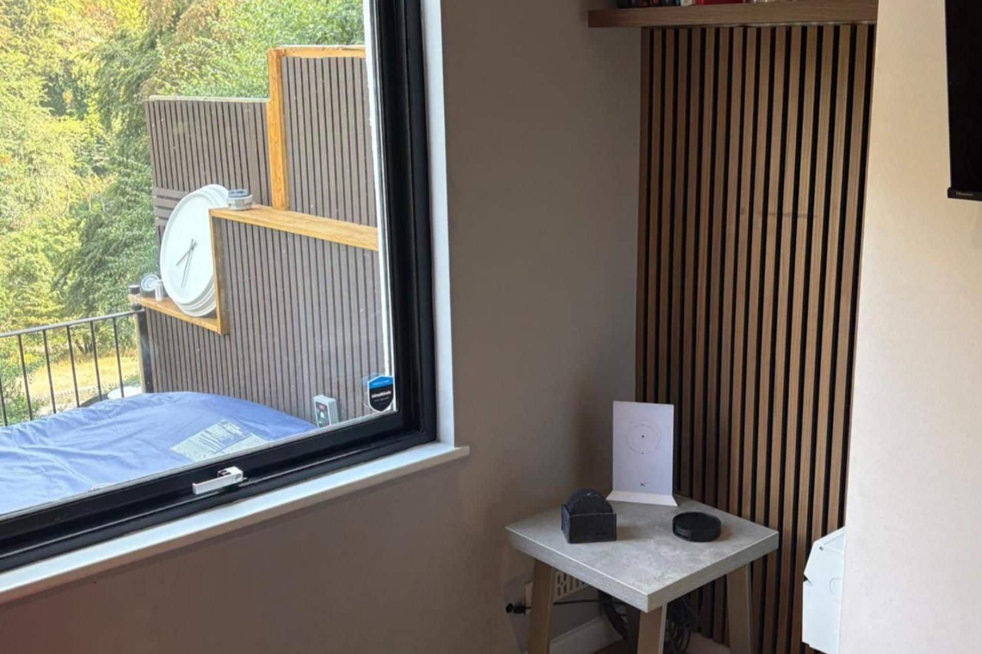 A room with a window, a small table, and a view of a wooden deck outside.