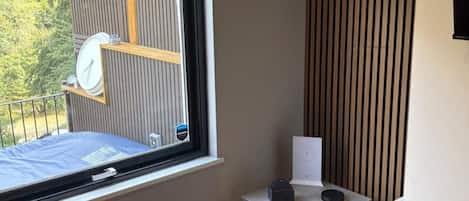 A room with a window, a small table, and a view of a wooden deck outside.