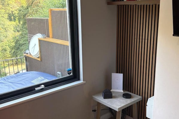 Una habitación con ventana, una mesita y vista a una terraza de madera.