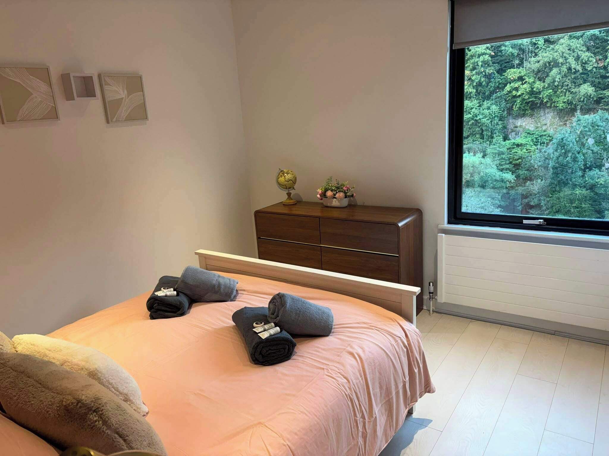 Ein Schlafzimmer mit Bett, einem Schminktisch, einem Fenster mit Blick auf Grünflächen und einem Globus auf dem Schminktisch.