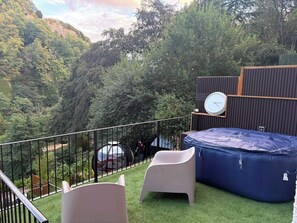 Een balkon met uitzicht op een bebost helling, een ronde tafel, twee stoelen en een blauwe opblaasbare luchtbed.