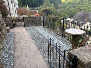 Un patio con un muro de piedra, una valla metálica y una mesa de madera.
