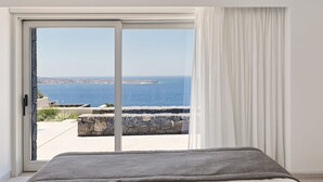 Ett sovrum med en stor skjutdörr i glas som leder ut till en balkong med utsikt över havet och en klippig kuststräcka.