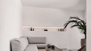 Ett minimalistiskt vardagsrum med en grå soffa, ett soffbord och en krukväxt.