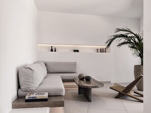 A minimalist living room with a grey sofa, a coffee table, and a potted plant. - Villa Elythiona, Divine Sea Views, Private Pool, Furnished Terrace, Sanrotini (Oia, Santorini)
