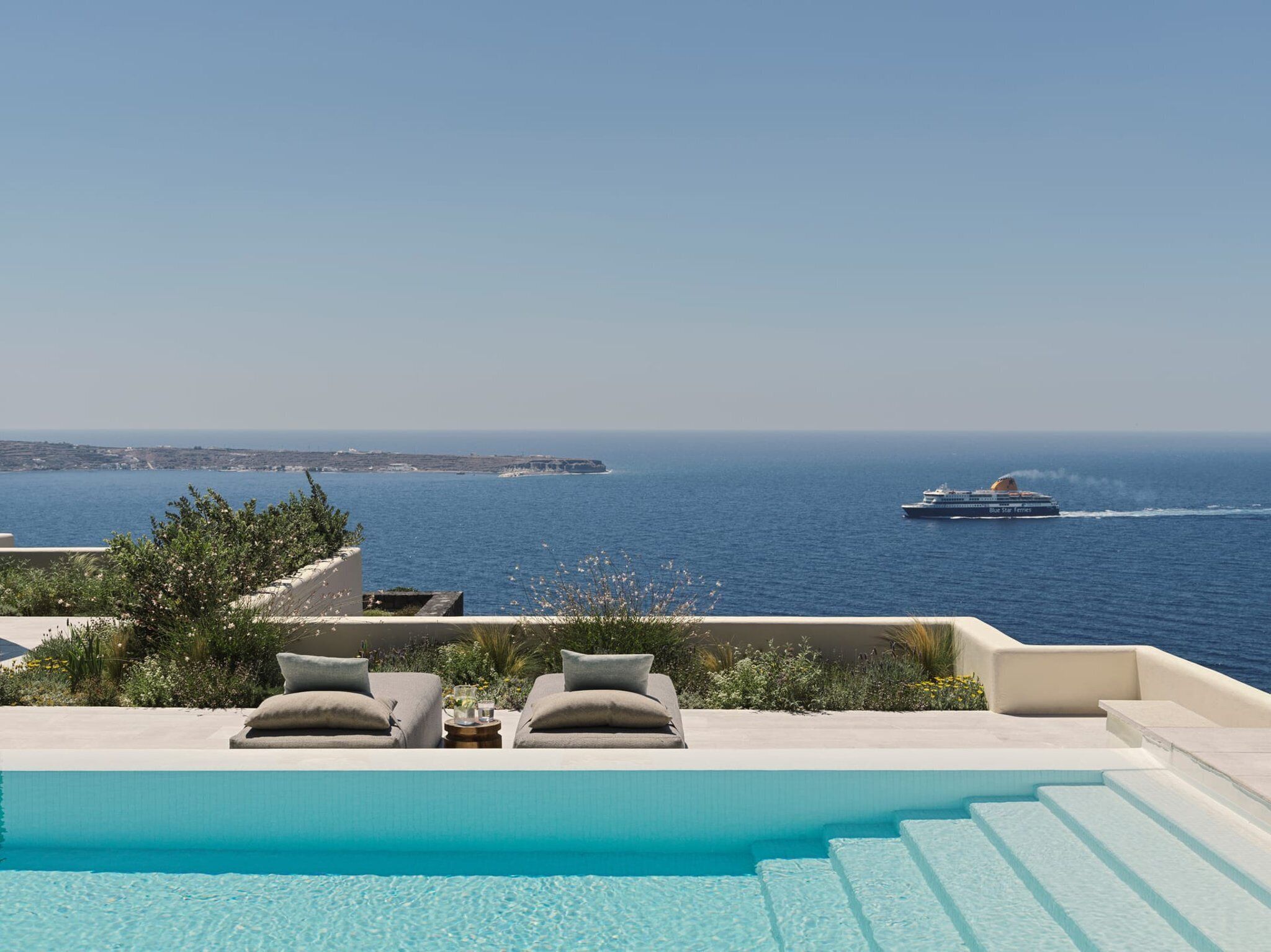 A pool with lounge chairs and a view of the sea and a cruise ship.