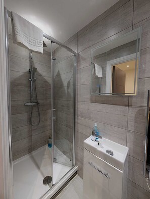 Een moderne badkamer met een douchecabine van glas, een wit wastafelmeubel en een spiegel.
