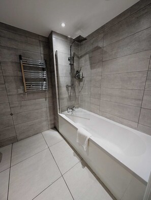 Een moderne badkamer met een bad, douche en handdoekhouder.