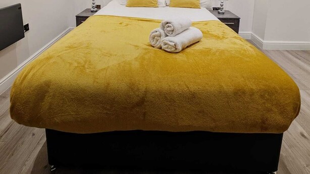 Un lit avec une couverture et des oreillers jaunes, deux tables de chevet avec des lampes et une tête de lit en bois.