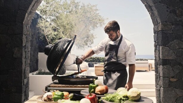 A chef grilling vegetables and meat in an outdoor kitchen with a stone archway. - Villa Solerion, Divine Sea Views, Private Pool, Furnished Terrace, Sanrotini (Oia, Santorini)