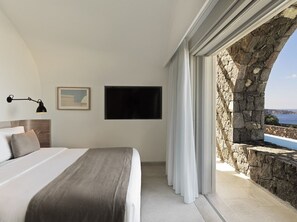 Un dormitorio con una cama, televisión de pantalla plana, un cuadro y pared de piedra con vistas.