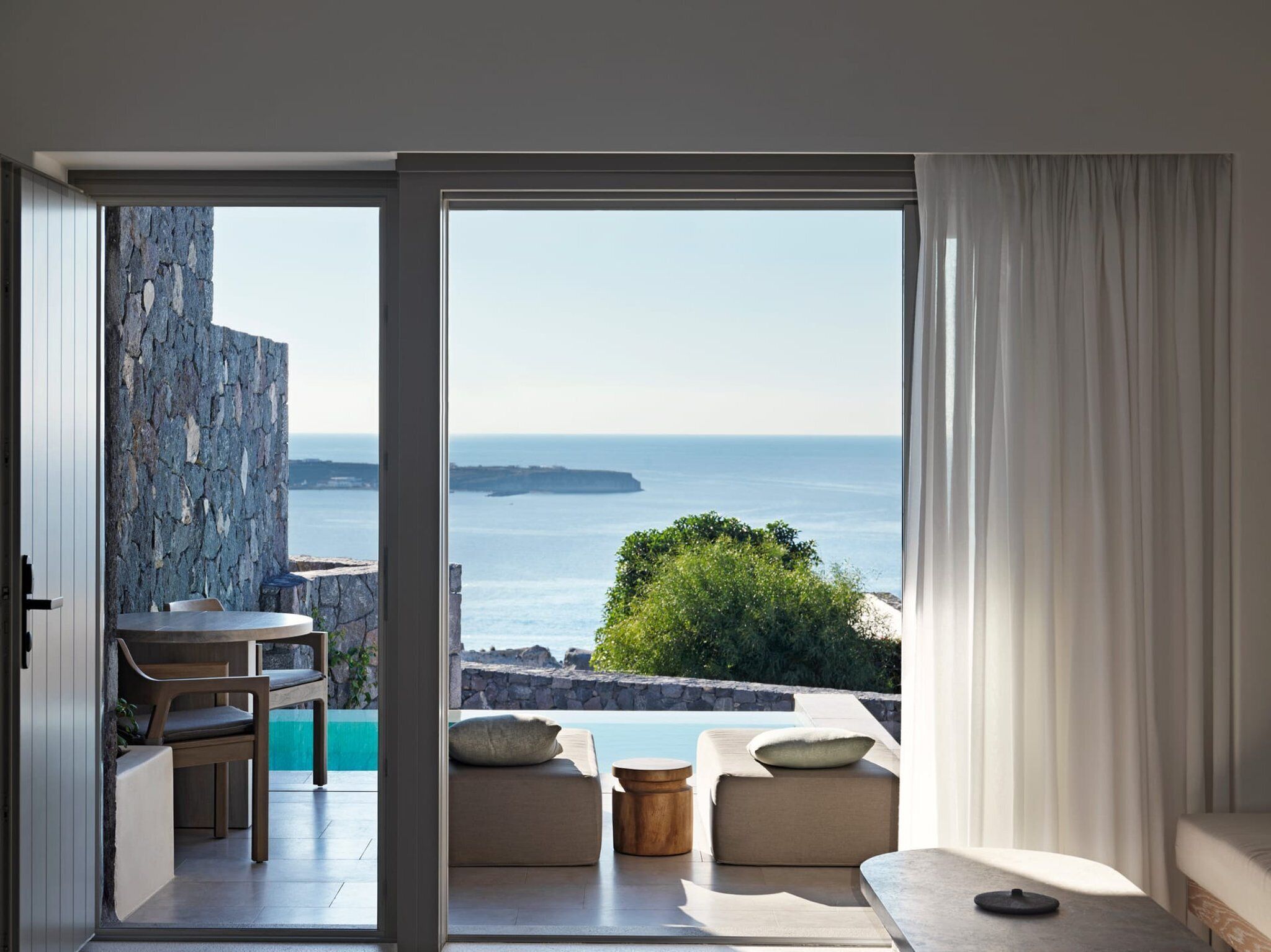 A modern room with a view of the sea, featuring a dining area, seating, and a large sliding glass door.