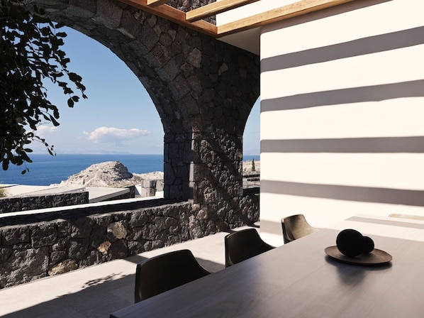 A dining area with a stone archway, a table, and chairs, overlooking a coastal landscape. - Villa Solerion, Divine Sea Views, Private Pool, Furnished Terrace, Sanrotini (Oia, Santorini)