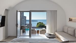 A modern bedroom with a large bed, a TV, and a view of the sea through an open door. - Villa Solerion, Divine Sea Views, Private Pool, Furnished Terrace, Sanrotini (Oia, Santorini)