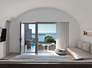 Ein modernes Schlafzimmer mit einem großen Bett, einem Fernseher und Meerblick durch eine offene Tür.