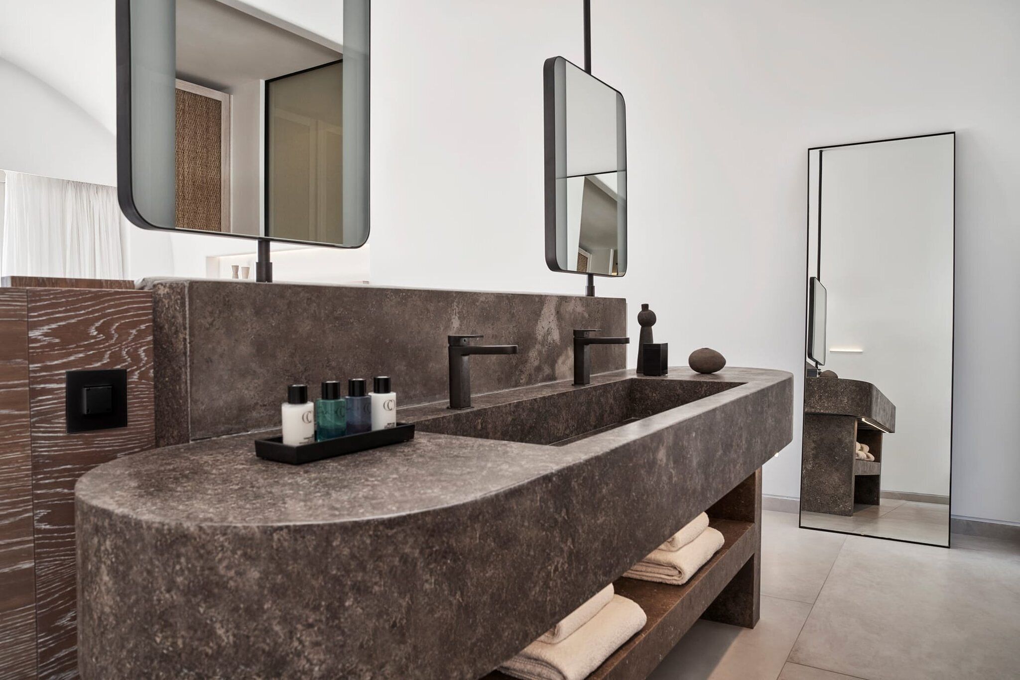 A modern bathroom with a curved granite sink, two black faucets, and a mirror above.