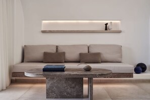 Een moderne woonkamer met een bank, kussens, een bijzettafeltje en een plank met decoratieve objecten.