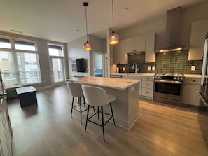 A modern kitchen with a central island, bar stools, a built-in oven, and pendant lighting. - Modern 1BR Bridge Park in Dublin with Balcony and Pool (Dublin)