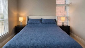 A bedroom with a large bed, two bedside tables with lamps, and a window with blinds. - Modern 1BR Bridge Park in Dublin with Balcony and Pool (Dublin)