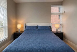 A bedroom with a large bed, two bedside tables with lamps, and a window with blinds. - Modern 1BR Bridge Park in Dublin with Balcony and Pool (Dublin)