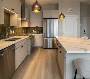 A modern kitchen with stainless steel appliances, a wooden floor, and pendant lighting. - Modern 1BR Bridge Park in Dublin with Balcony and Pool (Dublin)