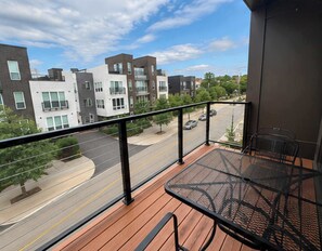 A balcony with a table and chairs, overlooking a street with modern buildings and a clear sky. - Modern 1BR Bridge Park in Dublin with Balcony and Pool (Dublin)