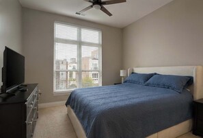 A bedroom with a bed, a television, a ceiling fan, and a window with blinds. - Modern 1BR Bridge Park in Dublin with Balcony and Pool (Dublin)