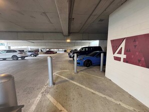 Ett underjordiskt parkeringsgarage med betongväggar, en vit vägg med ett geometriskt mönster och flera parkerade bilar, inklusive en blå sportbil.