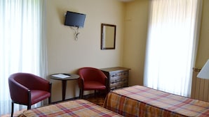 Una habitación de hotel con dos camas individuales, un escritorio con silla, un televisor montado en la pared y un aparador.