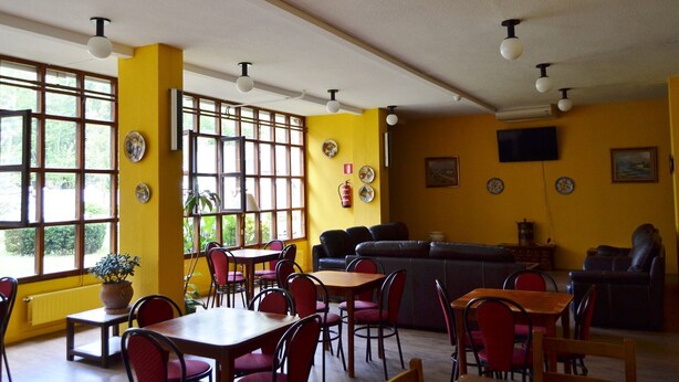 Un comedor con paredes amarillas, varias mesas y sillas, un sofá y un televisor fijado a la pared.