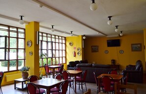 A dining area with yellow walls, multiple tables and chairs, a sofa, and a television mounted on the wall. - Termas de Lierganes (Liérganes)