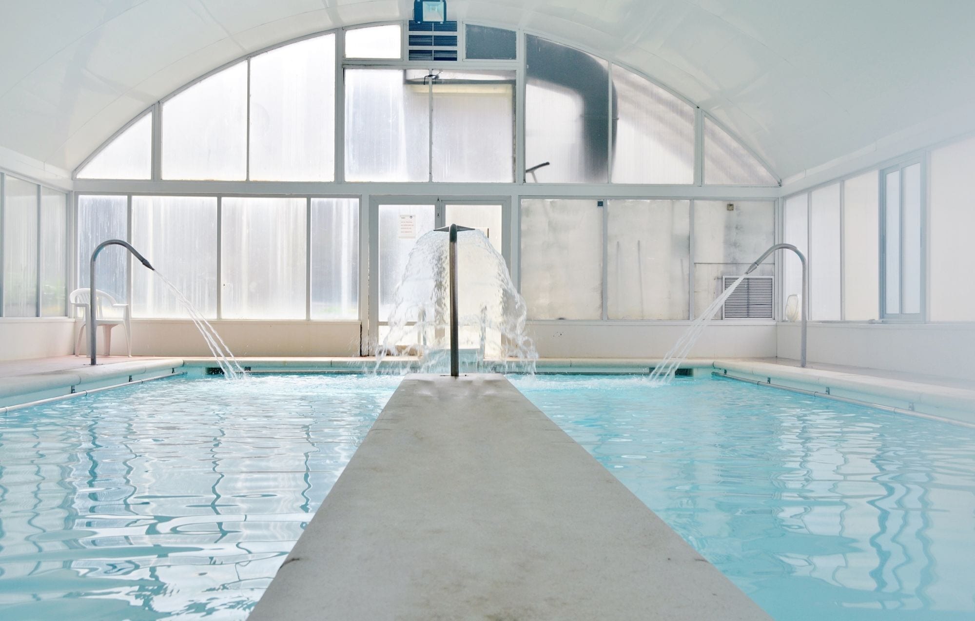 Una piscina coberta de forma llarga i estreta, envoltada d'ampies finestres i un sostre alt.