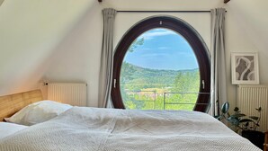 Quarto com uma grande janela, uma cama com manta texturizada, radiador e uma planta.