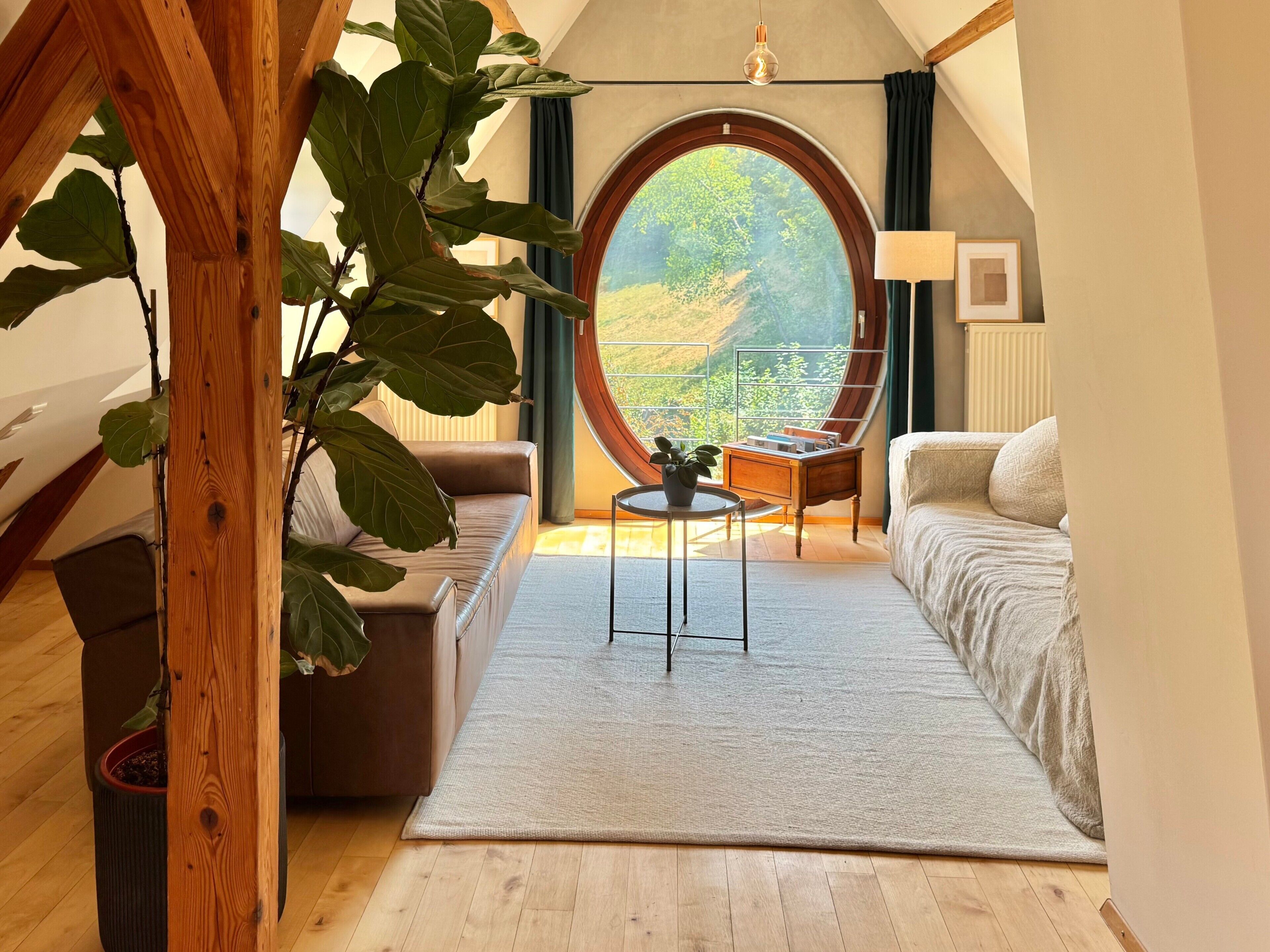A cozy room with a large round window, a sofa, a small table, and a potted plant.