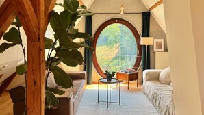 Um quarto acolhedor com uma grande janela redonda, um sofá, uma mesa pequena e um vaso de planta.