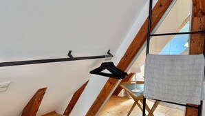Quarto com piso de madeira, um porta-bagagem de metal preto e uma toalha branca pendurada em uma barra de metal.