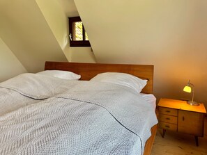 A bedroom with a wooden headboard, a single bed with white bedding, a nightstand with a lamp, and a small window. - Apartment 'In den Bäumen' – Quiet Apartment on the Edge of the Forest near Freiburg (Bollschweil)