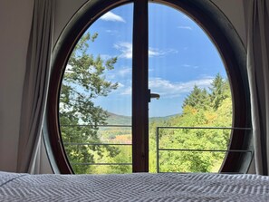 A room with a large circular window overlooking a forested landscape. - Apartment 'In den Bäumen' – Quiet Apartment on the Edge of the Forest near Freiburg (Bollschweil)