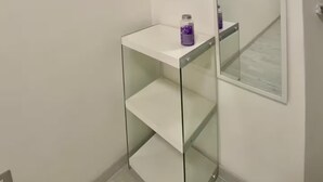 A bathroom with a white vanity, a mirror, and a glass shelf.